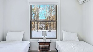 A bedroom with two beds, a window with a view of trees and snow, and a nightstand with a lamp. - Sunny Condo with Golf Views, Windsor Village (Hartford)