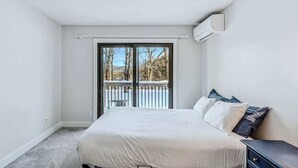 A bedroom with a bed, a nightstand, and a window overlooking a deck. - Sunny Condo with Golf Views, Windsor Village (Hartford)