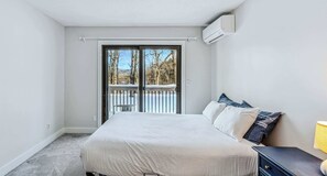 A bedroom with a bed, a nightstand, and a window overlooking a deck.