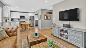 A modern living room with a leather sofa, wooden coffee table, and a flat-screen TV on a grey cabinet. - Cozy Collingwood Farmhouse, With Sauna (Collingwood)