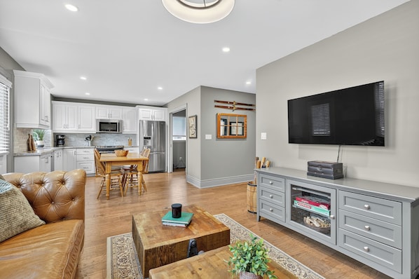 A modern living room with a leather sofa, wooden coffee table, and a flat-screen TV on a grey cabinet.