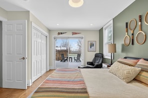 A bedroom with a bed, a chair, a desk, a lamp, and a view of the outside.