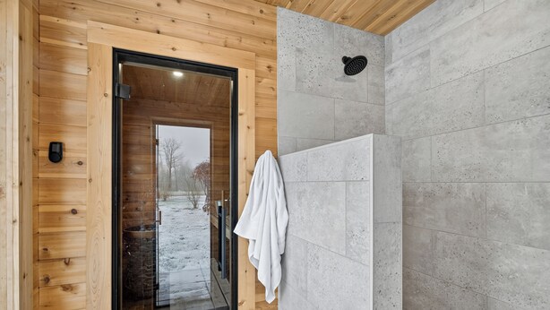 A wooden interior with a shower area, a glass door leading outside, and a towel hanging on the wall. - Cozy Collingwood Farmhouse, With Sauna (Collingwood)