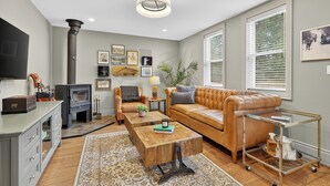 A living room with a fireplace, leather sofa, wooden coffee table, and a television. - Cozy Collingwood Farmhouse, With Sauna (Collingwood)