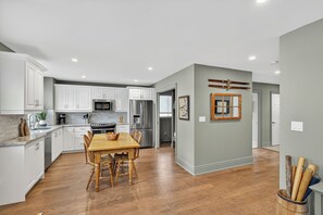 A modern kitchen with white cabinets, stainless steel appliances, and a wooden dining table.