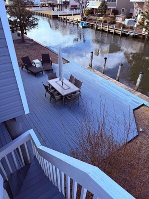 Une terrasse dotée de mobilier d’extérieur, une jetée s’avançant dans l’eau et une vue sur un quartier résidentiel.