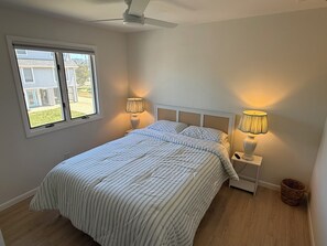 Une chambre à coucher avec un lit, deux lampes de chevet, un ventilateur de plafond et une fenêtre.