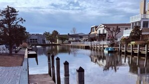 Un muelle de madera que se adentra en aguas tranquilas, reflejando casas cercanas.