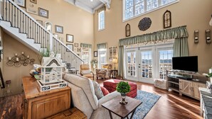 A spacious living room with a staircase, wooden flooring, and a large window offering a view. - Lake Views, Gym & Arcade | Gated | Sleeps 9 (Sevierville)