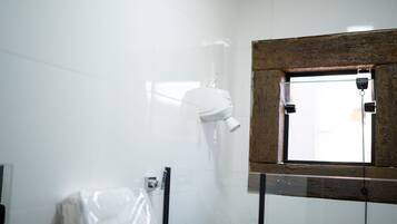 Een badkamer met witte tegels, een aan de muur bevestigde haardroger, een raam met houten kader en een douchegedeelte.