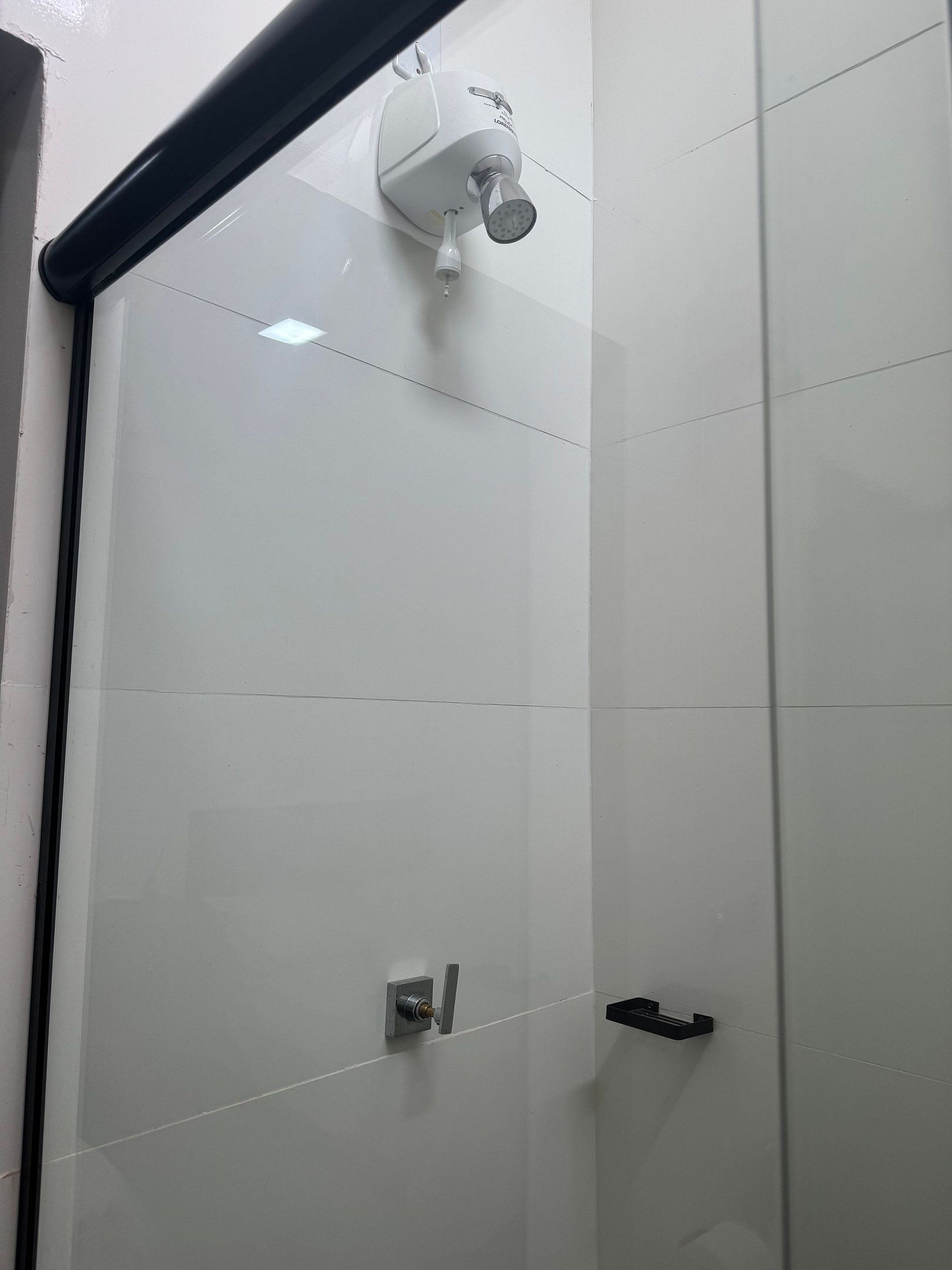 Baño con azulejos blancos, cabezal de ducha, grifo y toallero negro.