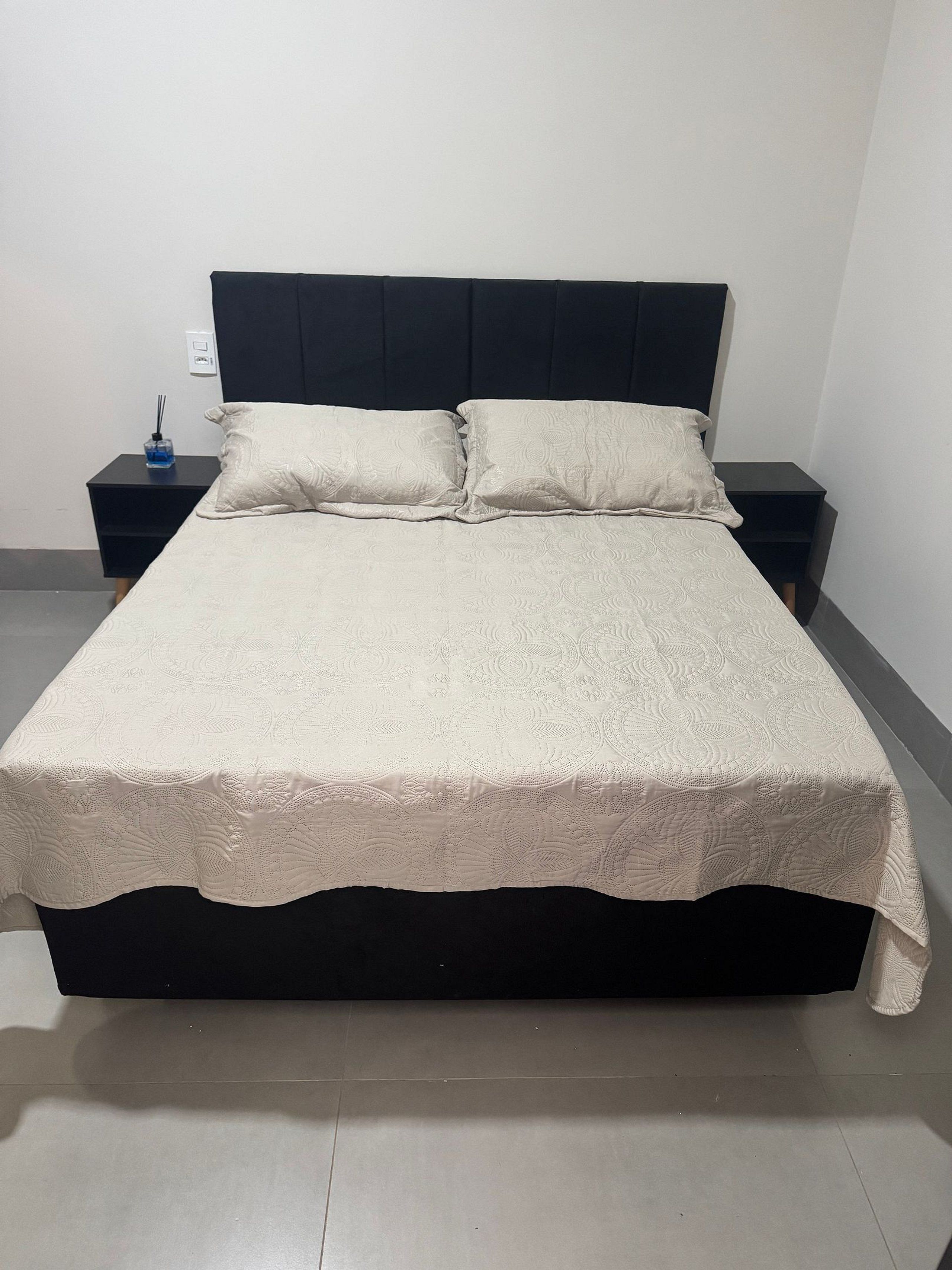 Een bed met een donker hoofdbord, twee nachtkastjes en een decoratieve spreidekker.