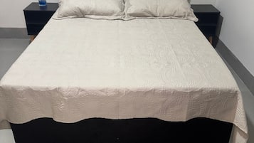 Una cama con cabecera oscura, dos mesitas de noche y una colcha decorativa.