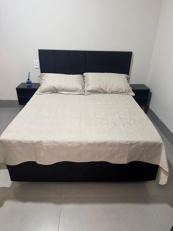 A bed with a dark headboard, two bedside tables, and a decorative bedspread.