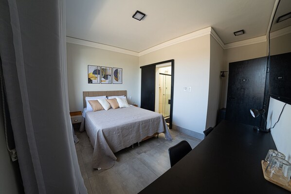 A bedroom with a bed, a desk, and a door leading to a bathroom. - POUSADA CARRO DE BOI (Lavras)