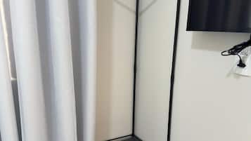A corner room with a black metal shelf unit, a flat-screen TV mounted on the wall, and a curtain partially covering a window.