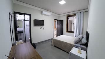 Habitación de hotel pequeña con cama, mesita de noche, televisor montado en la pared y baño a la vista a través de una puerta abierta.
