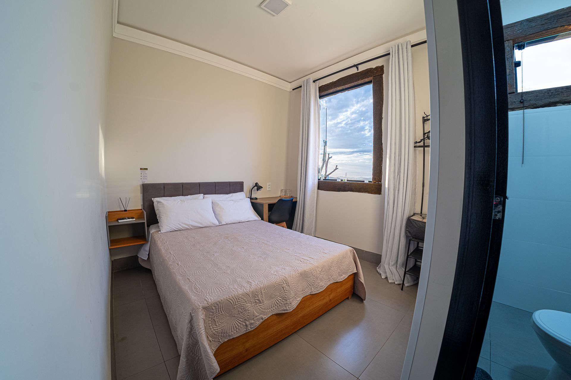 A bedroom with a bed, bedside table, lamp, and a window with curtains.