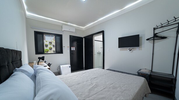 Un dormitorio con cama, mesita de noche, lámpara, equipo de aire acondicionado y televisor montado en la pared.