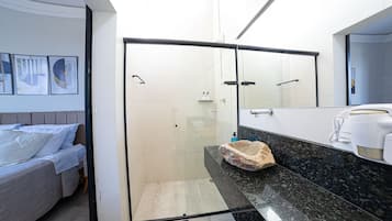 A modern bathroom with a glass shower enclosure, a marble countertop, and a bed with a headboard.