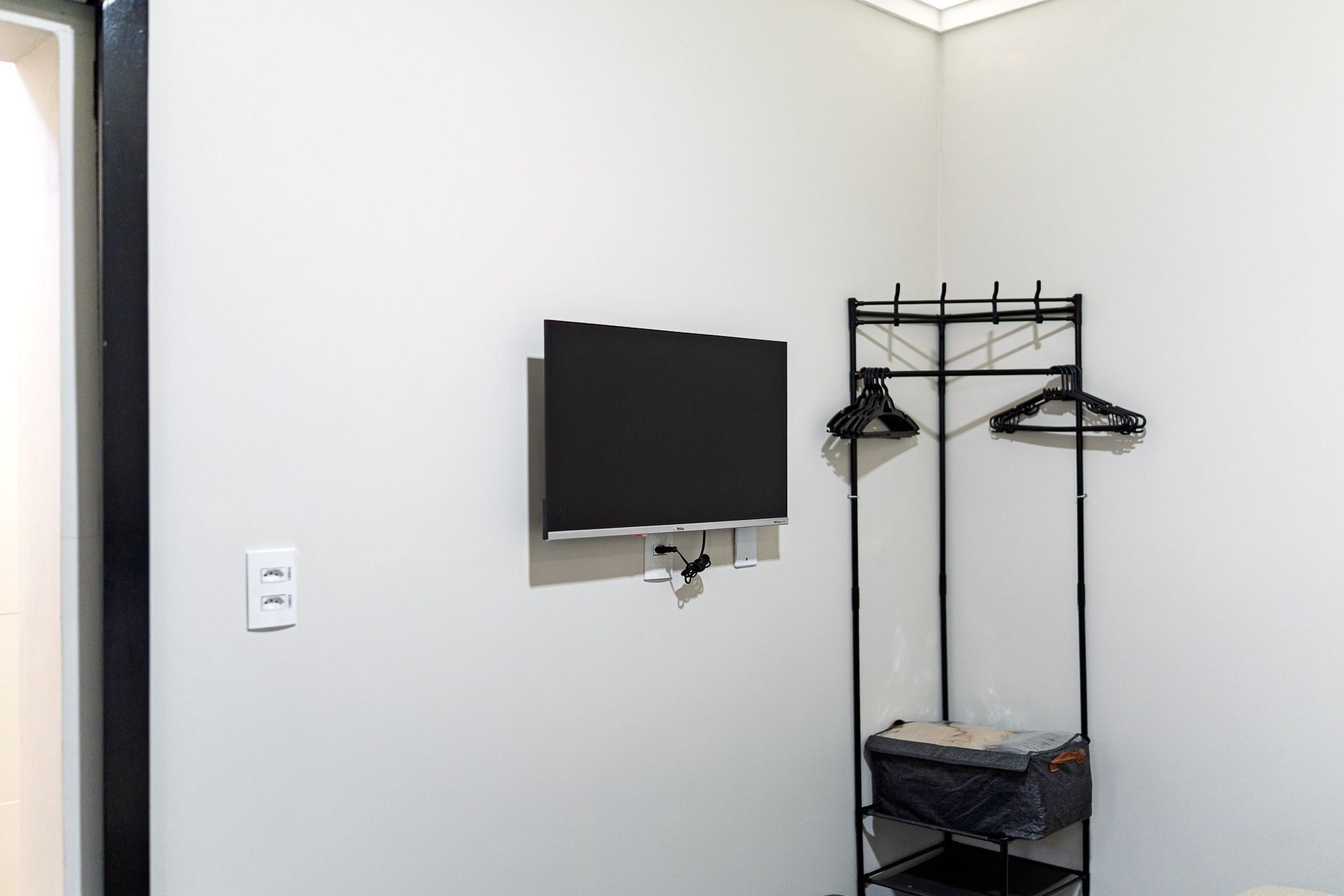 Una habitación con televisor de pantalla plana montado, perchero con ganchos y estante con un bolso.