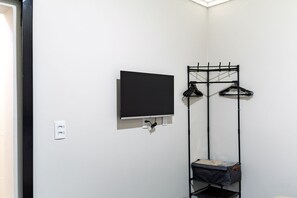 Una habitación con televisor de pantalla plana montado, perchero con ganchos y estante con un bolso.