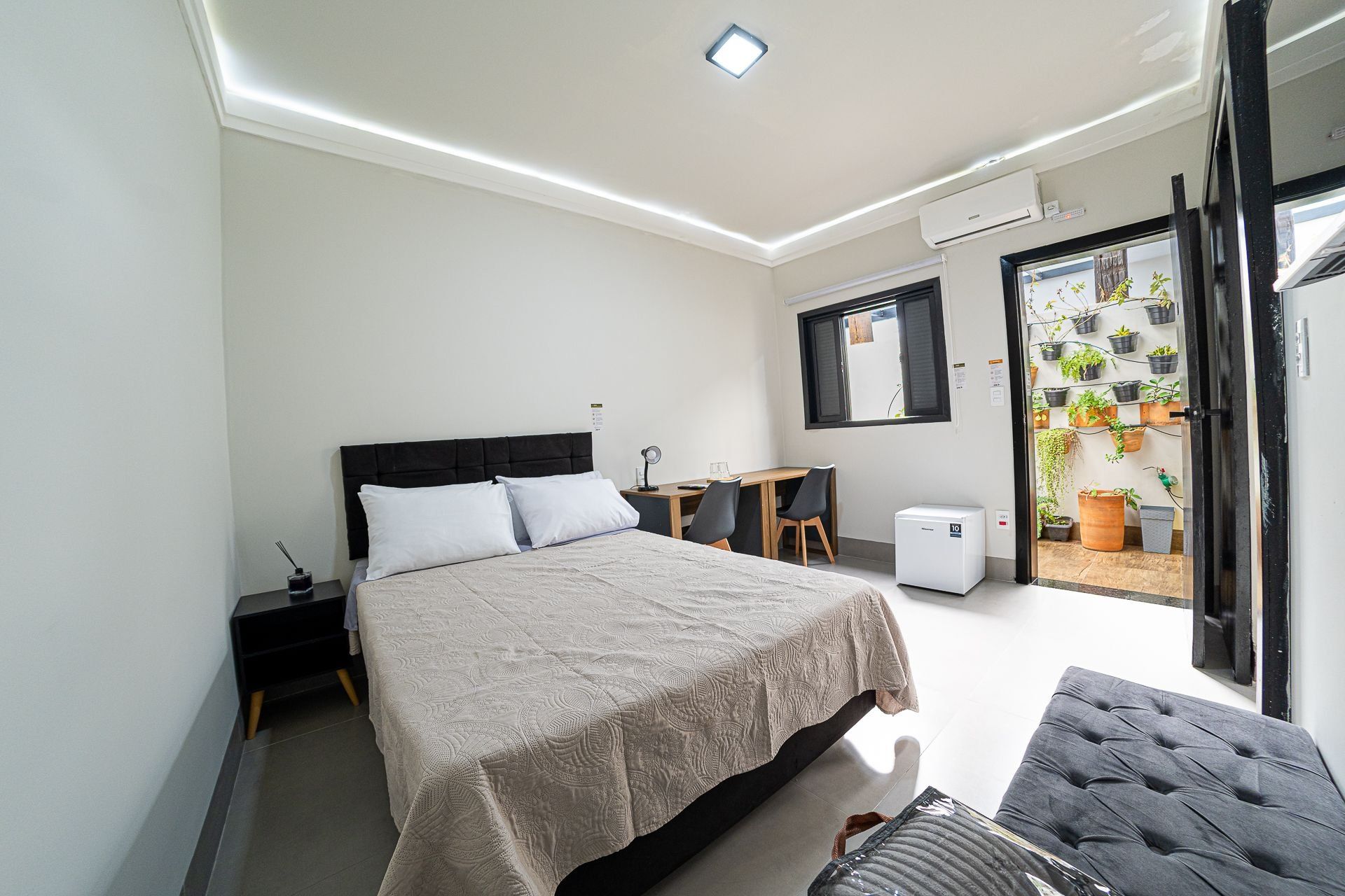 Um quarto moderno com cama, mesa de cabeceira, escrivaninha, cadeira e um pequeno aquecedor.