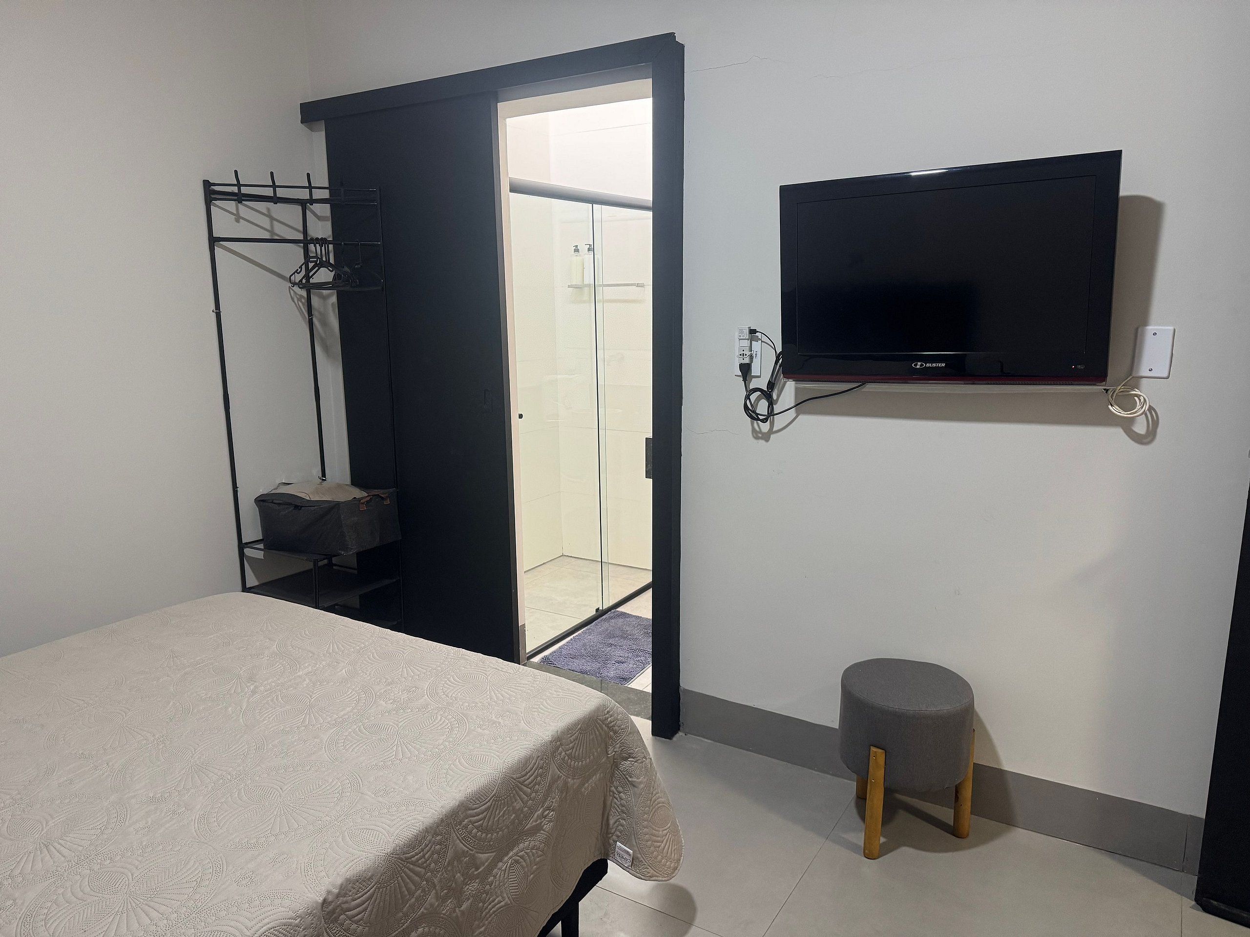 A room with a bed, a TV mounted on the wall, a small stool, and a door leading to a bathroom.