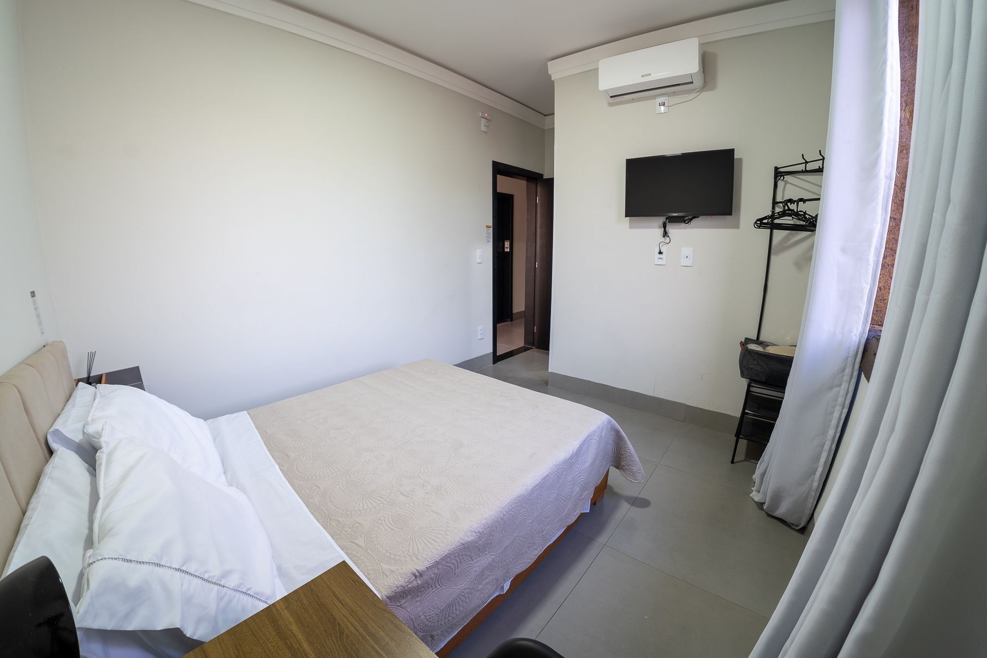 A hotel room with a bed, a television, an air conditioning unit, and a wardrobe.