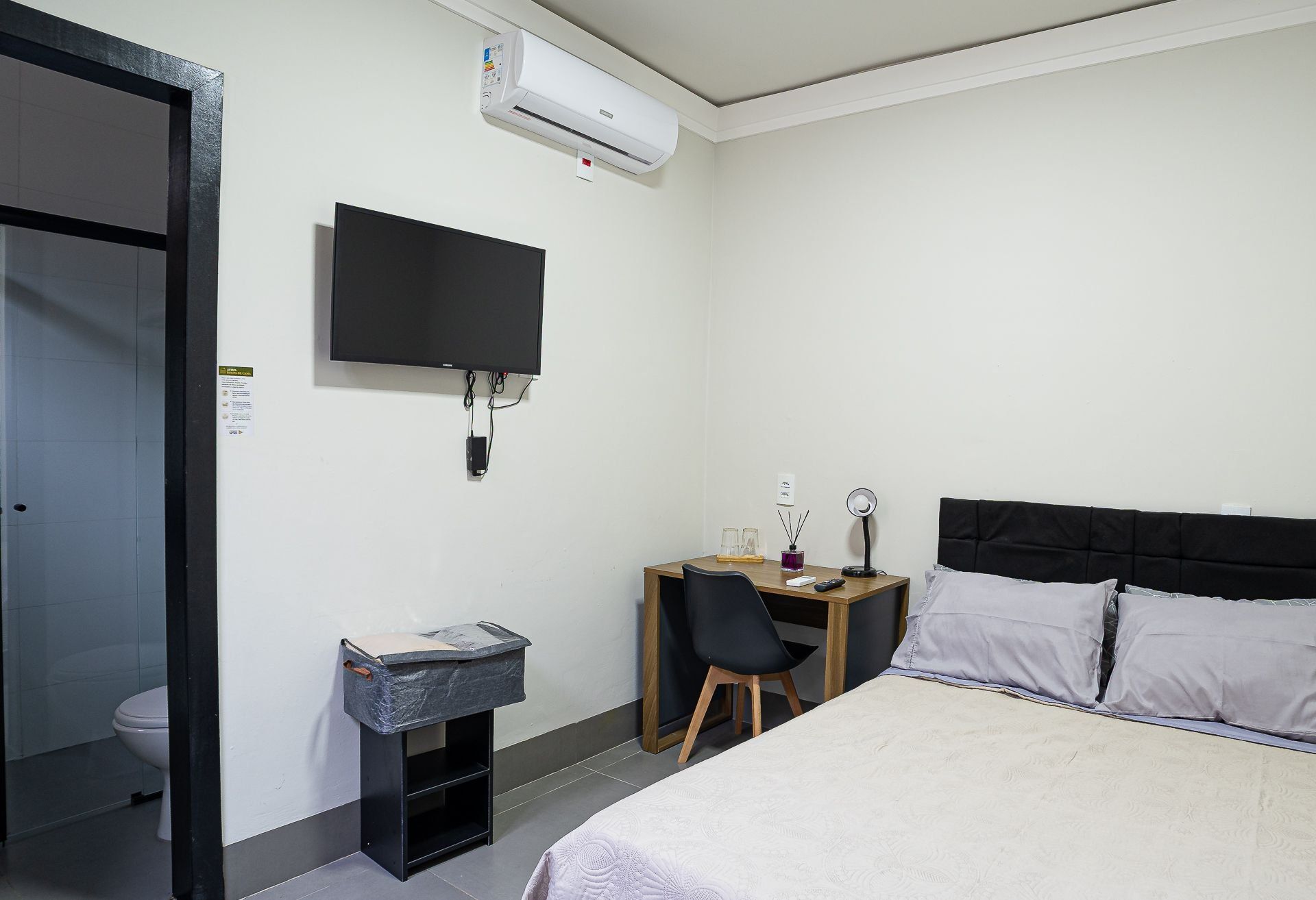 A hotel room with a bed, a desk with a chair, a television, and an air conditioning unit.