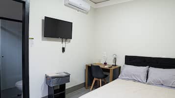A hotel room with a bed, a desk with a chair, a television, and an air conditioning unit.