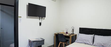 A hotel room with a bed, a desk with a chair, a television, and an air conditioning unit.