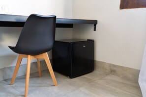 A compact kitchenette with a black refrigerator, a chair, and a wooden stool. - POUSADA CARRO DE BOI (Lavras)
