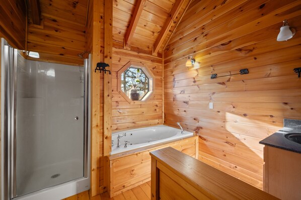 Une salle de bain rustique, aménagée dans une cabane en bois, avec une douche, une baignoire et une fenêtre ornée d’un objet décoratif suspendu.