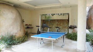 Une table de ping-pong installée à l’extérieur, avec un mur de pierres en arrière-plan et un pilier en pierre.