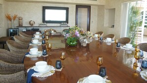 Une salle de conférence avec une longue table préparée pour une réunion, entourée de chaises en osier, et une grande fenêtre laissant entrer la lumière naturelle.