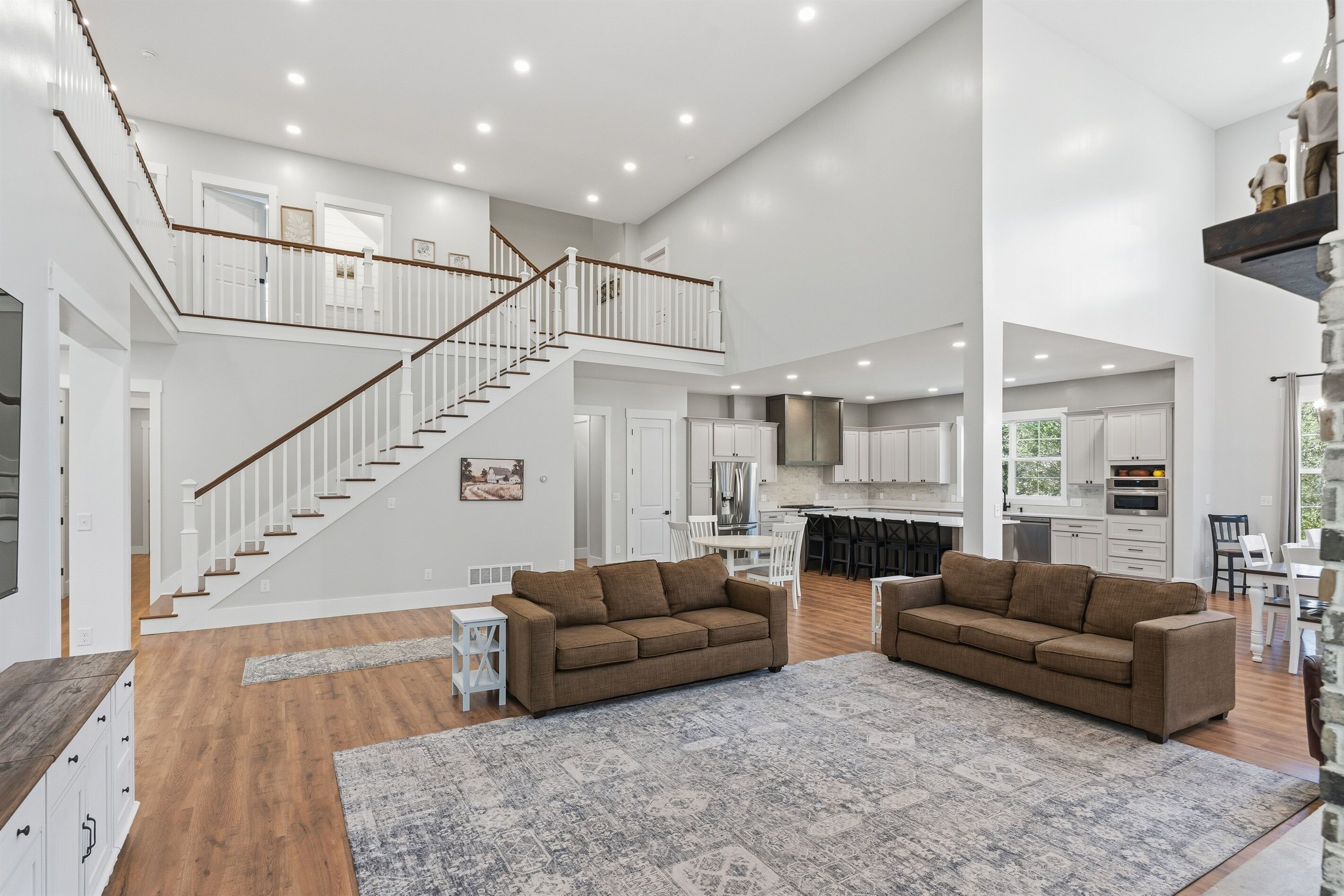 A spacious living area with a high ceiling, a staircase leading to an upper level, and a kitchen area visible in the background.