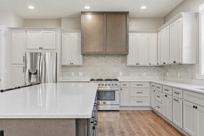 Une cuisine moderne avec des meubles blancs, un grand îlot central, des appareils en acier inoxydable et un dosseret carrelé.