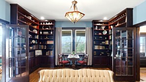 Una biblioteca con estanterías de madera oscura, un candelabro, un sofá y una mesa con sillas.