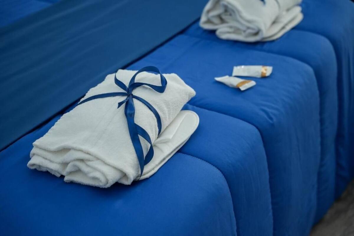 A hotel room with blue beds and a neatly folded white towel with a blue ribbon tied around it.