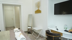 Hotellihuone, jossa on sänky, työpöytä, tuoli, televisio ja taulu seinällä.