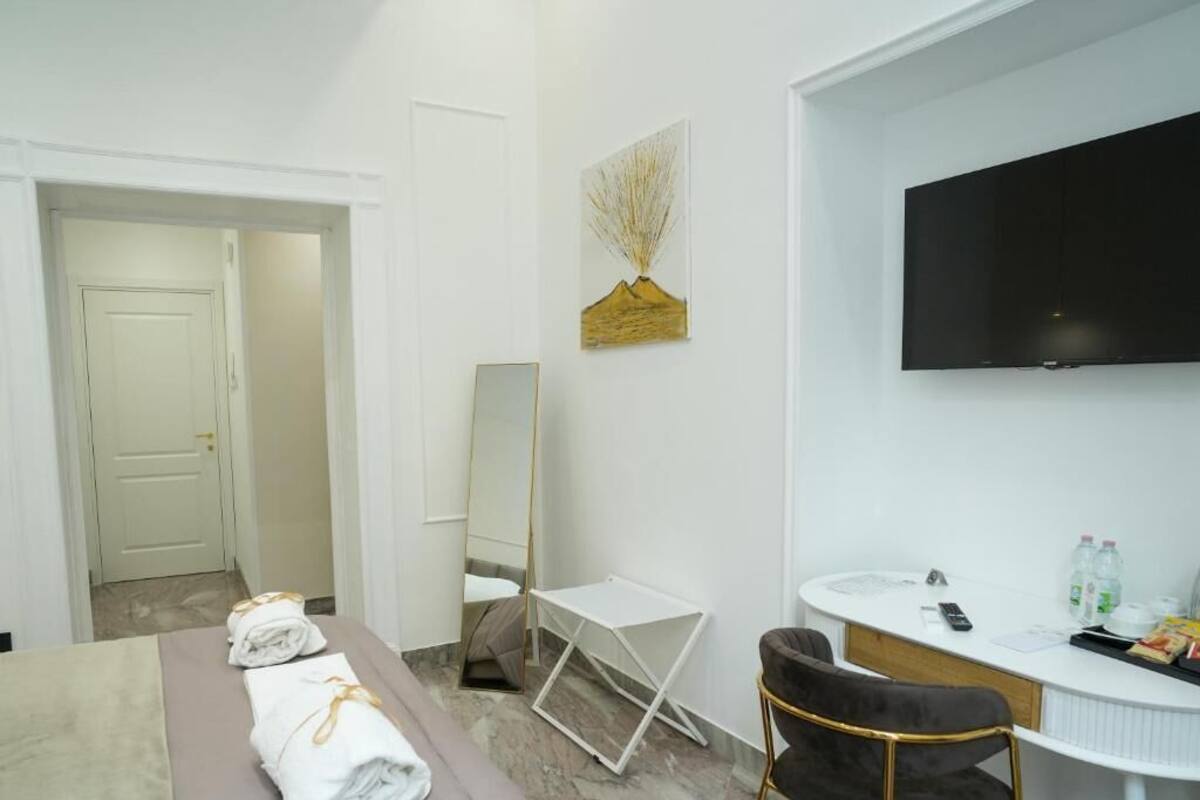 A hotel room with a bed, a desk, a chair, a TV, and a painting on the wall.