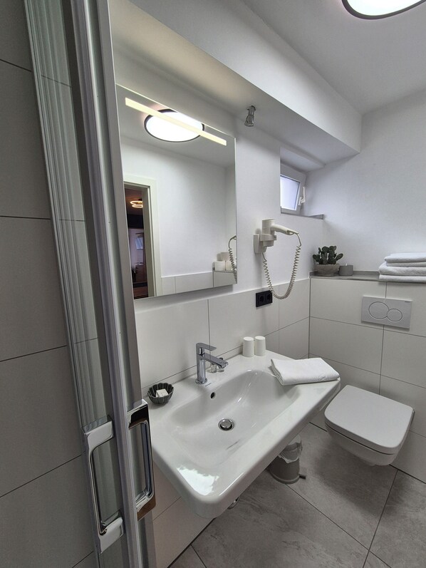 A modern bathroom with a large mirror, a sink, a toilet, and a hairdryer mounted on the wall.