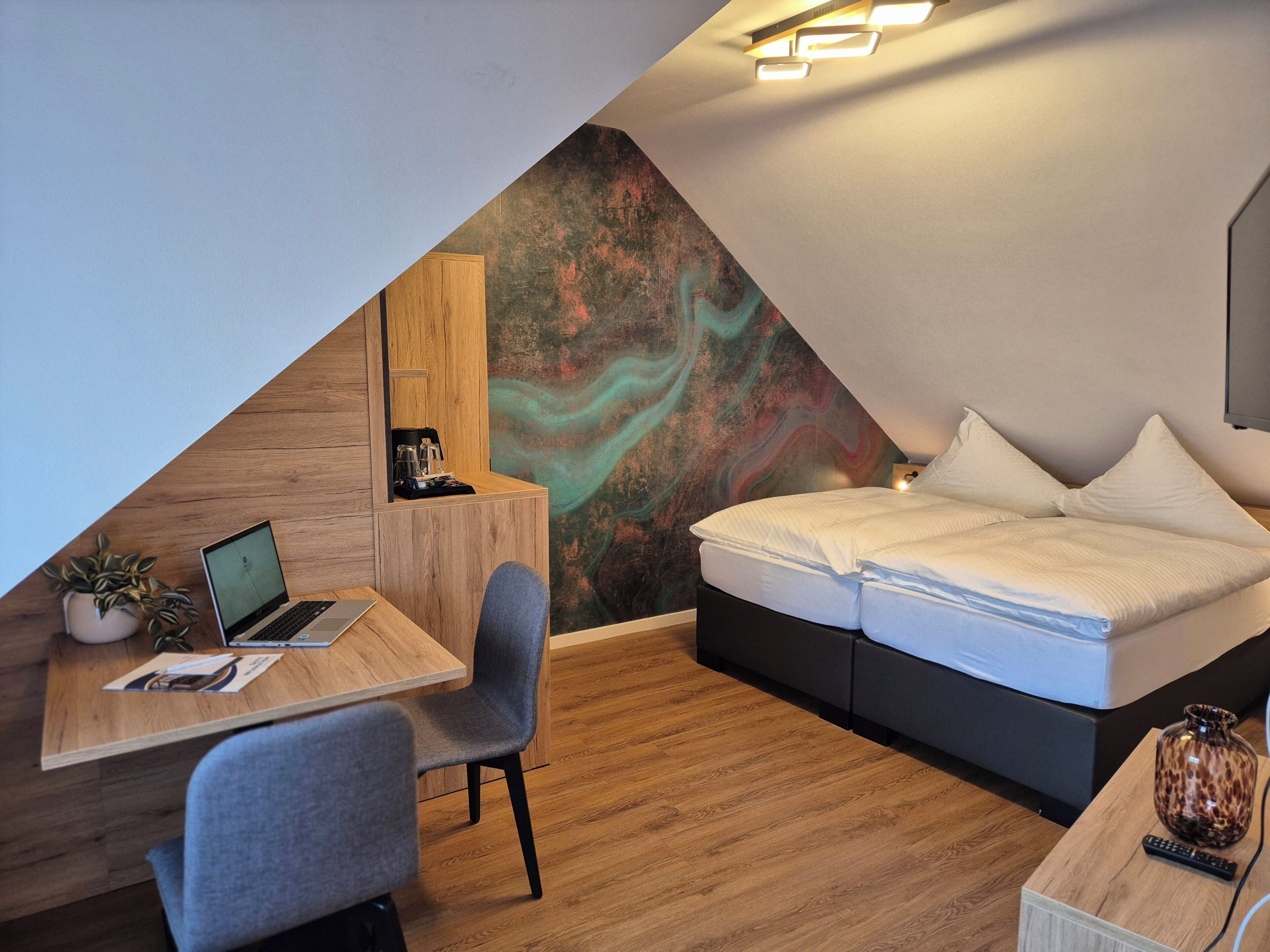 A modern room with a desk, chair, laptop, bed, and a unique wall mural.