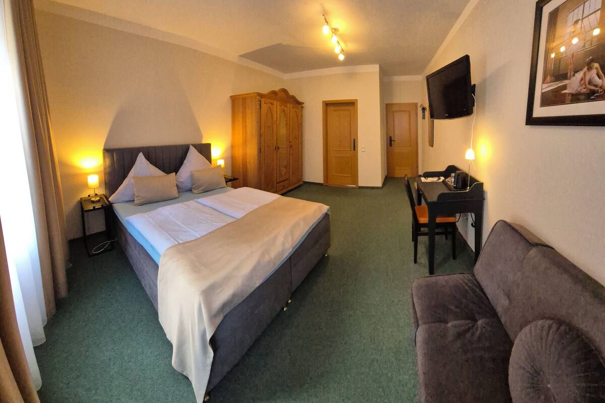 Une chambre d’hôtel comprenant un lit, des tables de chevet, une armoire, une télévision, un bureau et un canapé.