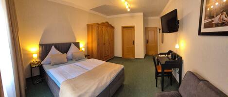 A hotel room with a bed, bedside tables, a wardrobe, a television, a desk, and a couch.