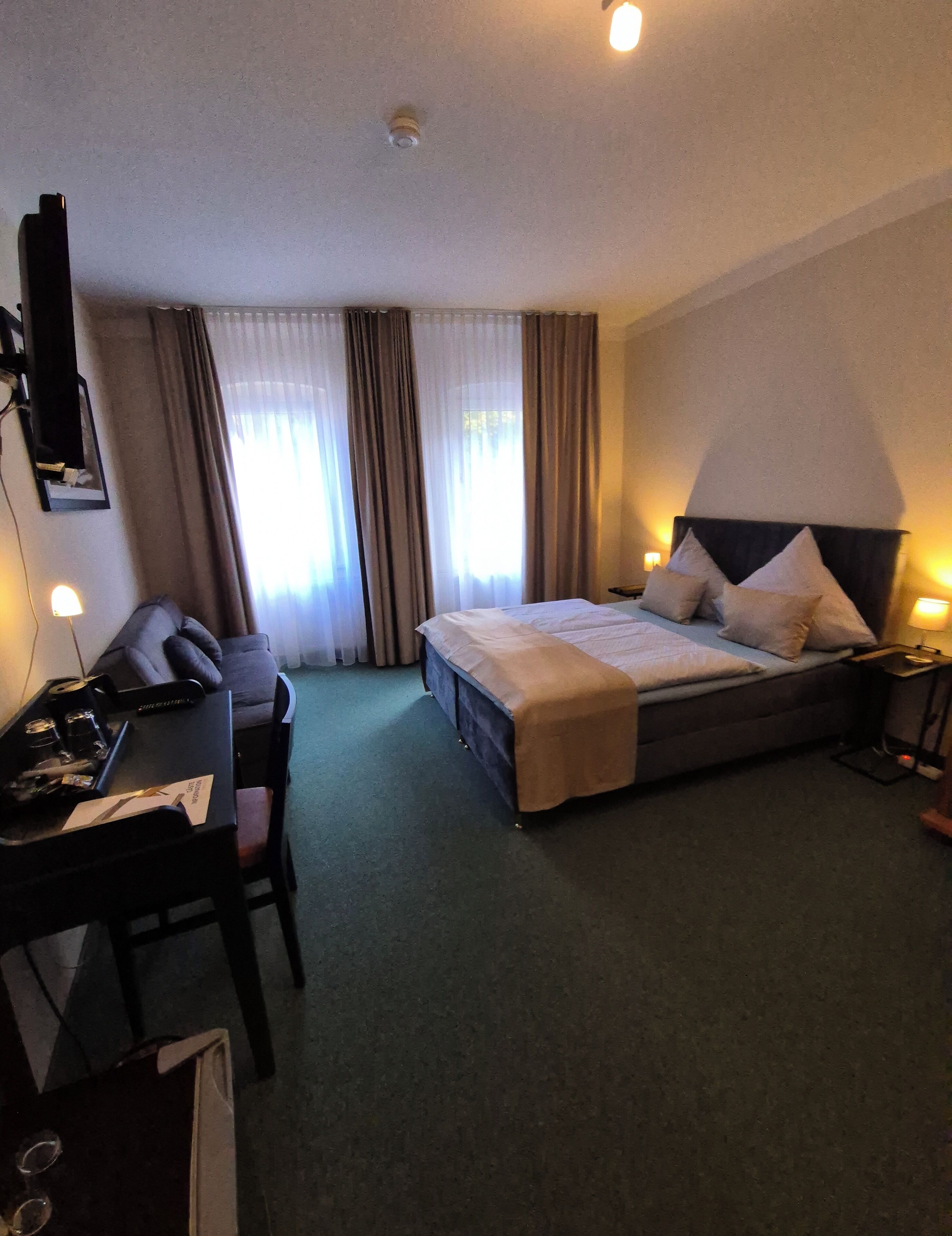 Habitación de hotel con cama, mesitas de noche, un escritorio con silla, televisión y cortinas.