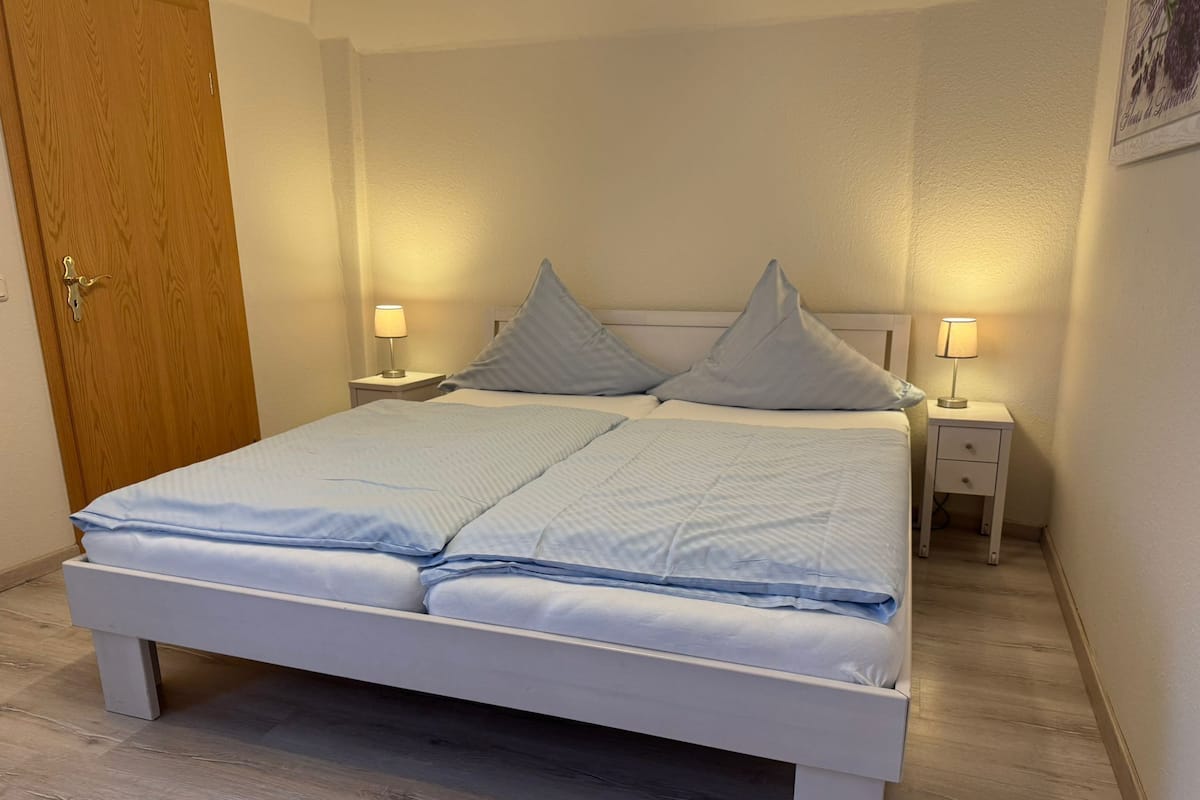 Un lit avec un cadre blanc, deux tables de chevet avec des lampes et une porte en bois.