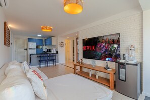 A modern living room with a large flat-screen TV, a compact fridge, and a cozy seating area.