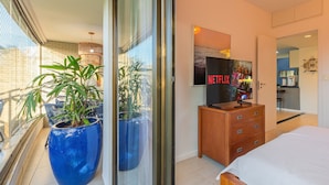 A hotel room with a bed, a wooden dresser, a television displaying 'NETFLIX', and a large blue potted plant. - Beach Place #202 - Seafront by Carpediem (Aquiraz)